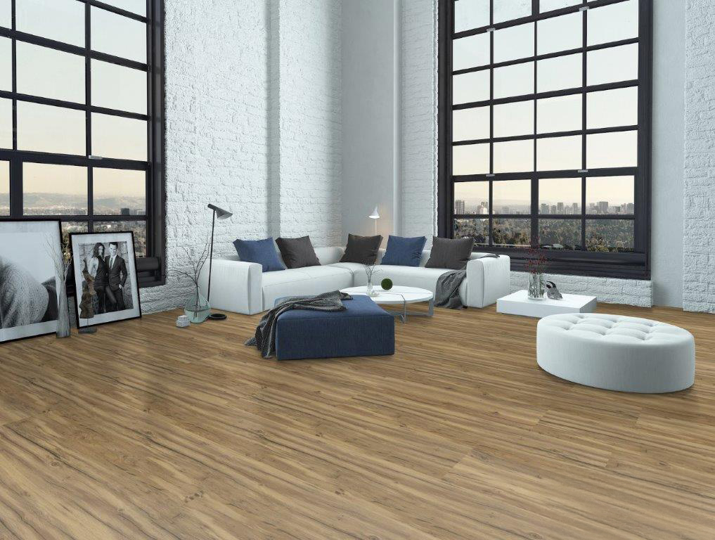 Modernes Loft-Wohnzimmer mit großen Industriefenstern, weißen Backsteinwänden, einem weißen Sektionssofa mit grauen Kissen, einer runden weißen Ottomane, einem blauen Fußhocker und gerahmten Fotos, die auf dem Boden vor der Wand stehen.